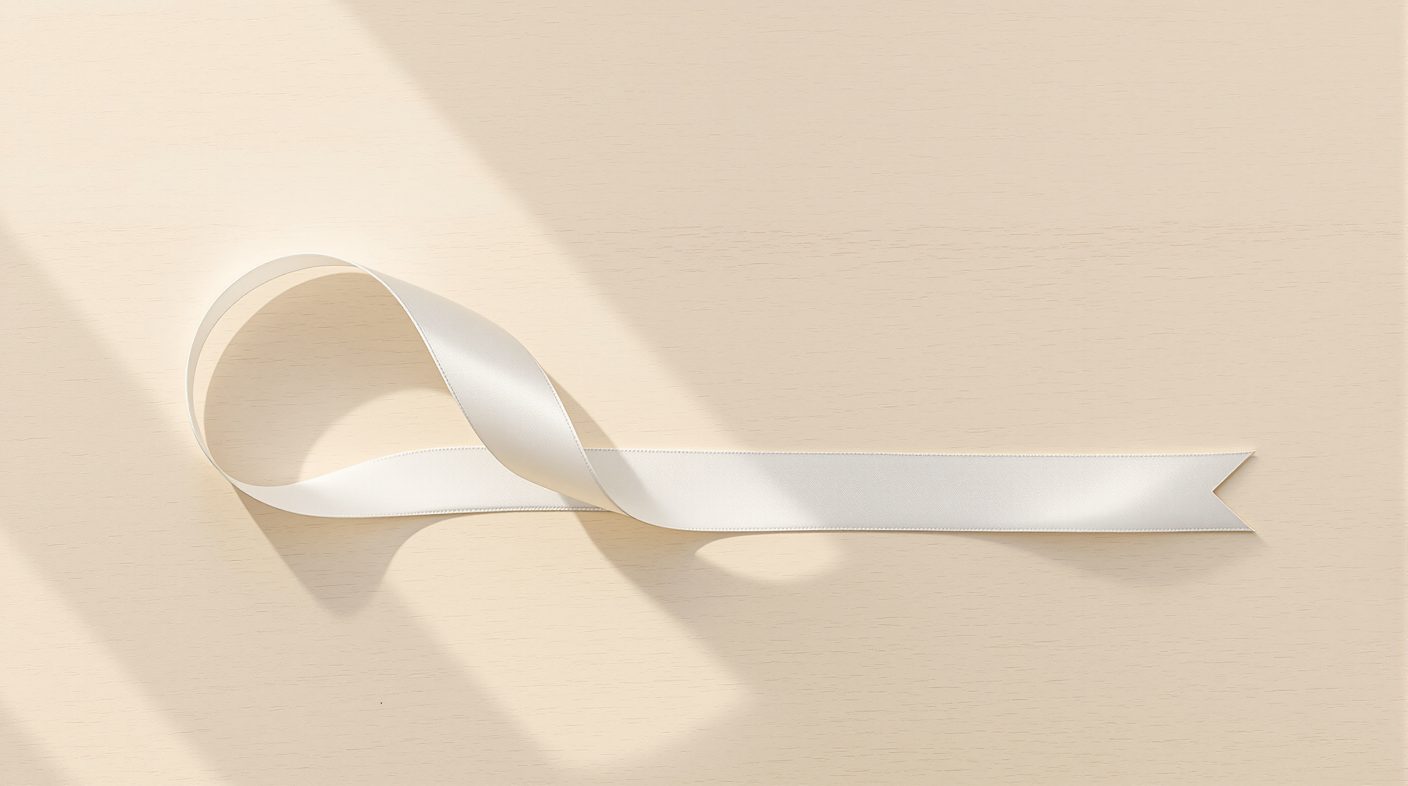 A length of pale silk ribbon curving across a pale wooden table, low warm sunlight crossing it from a window